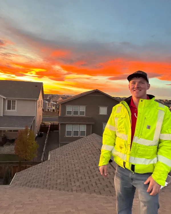 Evan on a roof at sunset in a high-visibility jacket over a red Christmas Lights Professionals polo