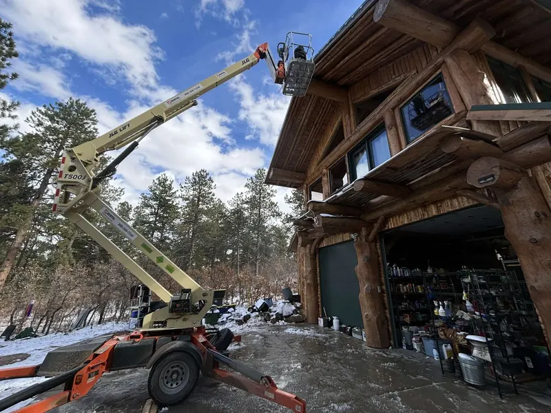 Boom lift raised beside a tall log home during one of our installs