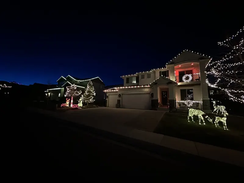 Home with roofline lights, wrapped trees and lit reindeer on the lawn