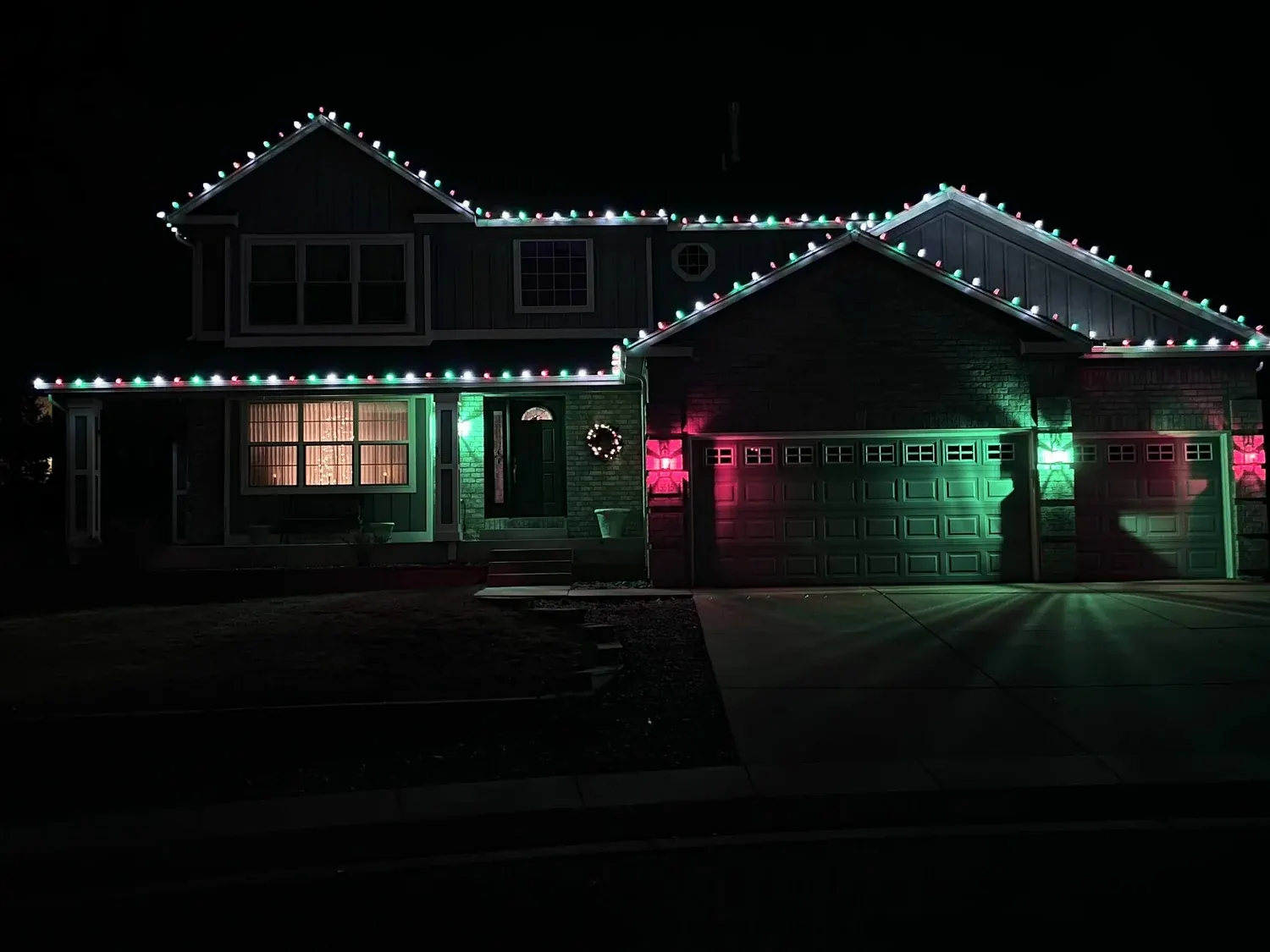 Two-story home with red, green and white Christmas lights along every roofline