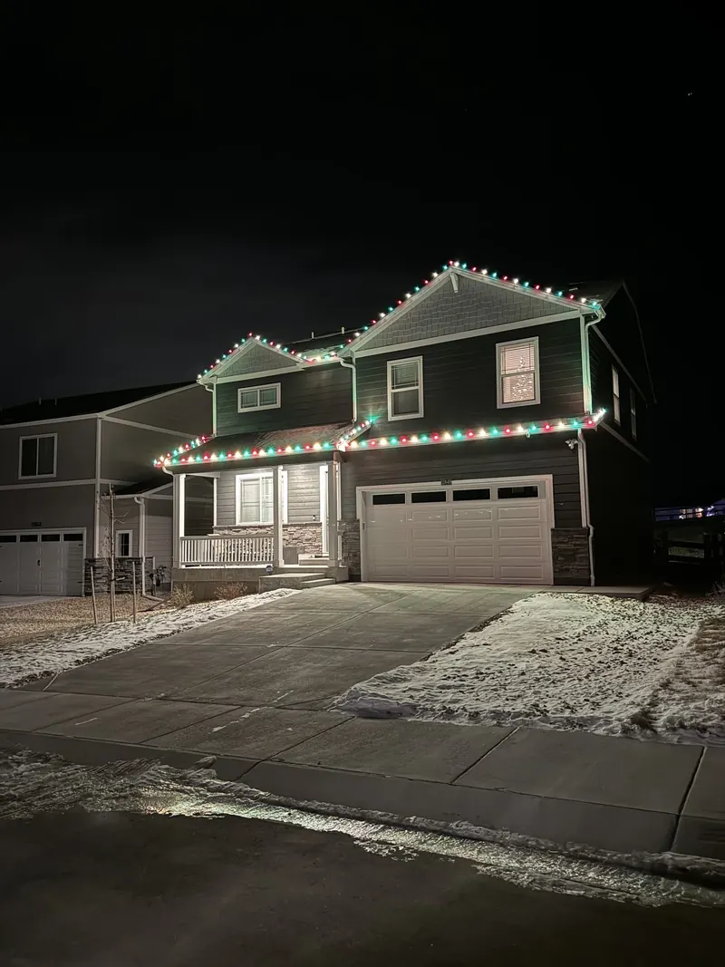 Two-story home with red and white lights after a snowfall